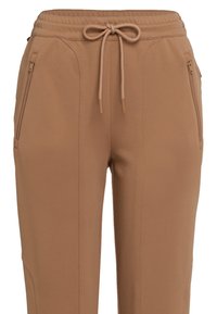 Brown tapered pants with front zipper pockets and a drawstring knot at the elastic waistband, shown from waist to mid-thigh.