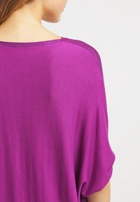 Magenta överdimensionerad topp med en mjuk textur, med subtil kontrasterande infällningar längs halsringningen och axelsömmarna. Löst sittande design.