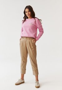 Lichtroze sweatshirt met "MY FOREVER DAY" in kleurrijke tekst, gecombineerd met beige cropped broeken en beige sneakers met een gestructureerde zool.
