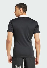 Polo shirt nero a maniche corte con colletto bianco; tessuto liscio; design slim; dettagli di cucitura discreti; indossato con pantaloni corti neri con logo.
