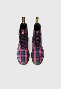 Bottines lacées à carreaux noirs et roses avec des coutures jaunes et une languette de tirage, présentant un upper en tissu texturé et une semelle en caoutchouc.