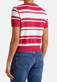 Červenobílý pruhovaný pletený top s krátkým rukávem a žebrovaným výstřihem a lemem, doplněný modrými džíny s zadními kapsami.