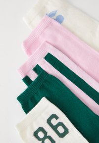Firet foldede sokker i hvit, rosa med grønne striper, ensfarget grønn, og hvit med nummer 86 på hvit bakgrunn.