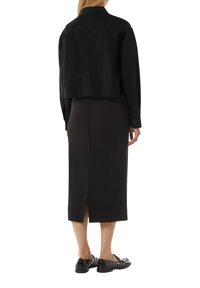 Skrócona czarna kurtka z kołnierzem, zestawiona z długą czarną spódnicą z rozcięciem z tyłu. Czarne loafersy dopełniają całość stylizacji.