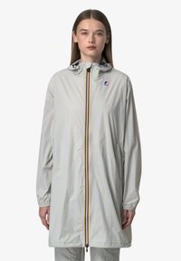 Giacca impermeabile grigio chiaro con cappuccio, dotata di chiusura frontale con zip, polsini elasticizzati e una striscia colorata al centro.