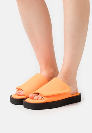 Οι πορτοκαλί σαγιονάρες διαθέτουν ευρύ, διπλωτό επάνω μέρος και παχύ μαύρο πέλμα, με ανοιχτό σχέδιο στο δάχτυλο για αναπνευσιμότητα.