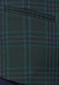 Zielona i granatowa tkanina w kratę o subtelnej fakturze, z prostą kieszenią wzdłuż górnej krawędzi. Wzór zawiera przecinające się linie.