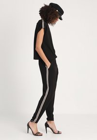 Svart kortärmad topp med vita ränder på axlarna, kombinerad med svarta byxor med sidoree; högklackade sandaler kompletterar looken.