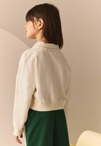 Cremefarvet sweatshirt med en afslappet pasform, ribbede manchetter og en rund halsudskæring, parret med grønne bukser. Blød tekstur, afslappet design.