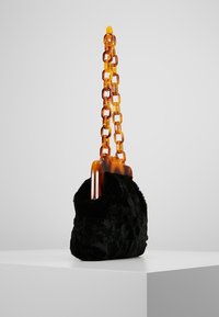 Černá kabelka z umělé kožešiny s ambrovým želvovinovým řetízkovým uchopem. Měkká textura, zaoblený tvar a výrazné detaily s kovovými prvky.