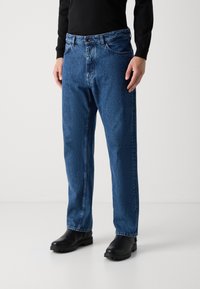 Jeans de mezclilla azul con un ajuste relajado, diseño de cinco bolsillos y cremallera. La tela tiene un acabado ligeramente texturizado y un lavado medio.