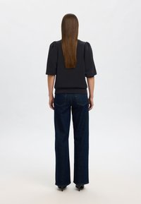 Svart blus med puffärmar kombinerad med mörkblå vida jeans. Mjuk tygstruktur med figursydd midja och subtila sömnadsdetaljer.