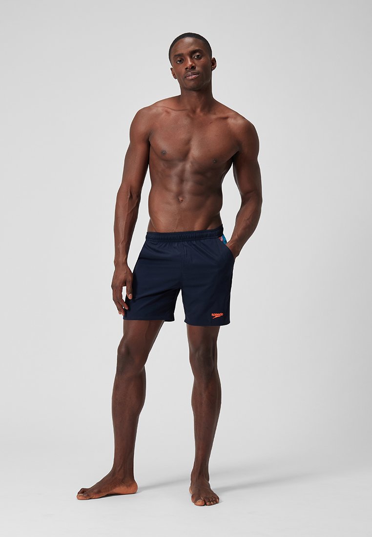 Granatowe kąpielówki z elastycznym pasem, pomarańczowym logo i bocznymi kieszeniami; wykonane z lekkiego, gładkiego materiału dla komfortu i swobody ruchów.