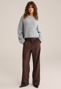 Sivi skrajšan pulover iz teksturiranega pletenja, v kombinaciji s smešnimi širokimi hlačami rjave barve s pikastim vzorcem in črnimi špičastimi čevlji. Preprost dizajn, sproščen kroj.