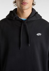 Felpa nera in cotone con tasca a marsupio frontale, cordoncini rotondi e un piccolo logo bianco sul petto. Morbido al tatto, vestibilità comoda.