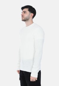 Maglione bianco lavorato a maglia con scollo rotondo, maniche lunghe e polsini a costine. Il tessuto presenta un motivo strutturato, adatto per abbigliamento informale.