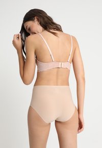 Bralette de renda rosa claro com alças ajustáveis e fecho de gancho, combinado com cuecas nude de cintura alta, textura suave e sem costuras visíveis.