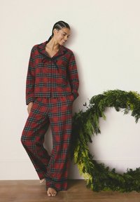 Rote karierte Flanell-Pyjama-Set mit einem Button-up-Oberteil mit Kragen und passenden Hosen. Weiche Textur mit grünen und schwarzen Akzenten.