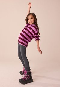 Lila und burgunderrot gestreifter Pullover, graue Leggings, schwarze Stiefel mit pinken Schnürsenkeln. Der Pullover hat einen Kragen und hochgekrempelte Ärmel.