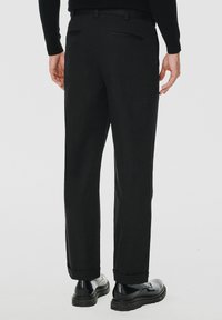 Czarne spodnie o prostym kroju, z dwoma tylnymi kieszeniami, z mankietami i gładką teksturą. Noszone z czarnymi butami.