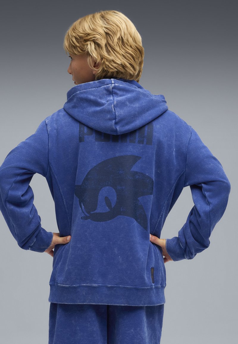 Felpa blu realizzata in morbido tessuto, con una grande grafica nera di un riccio e la parola "PUMA" sul retro. Inclusi maniche lunghe e cappuccio.