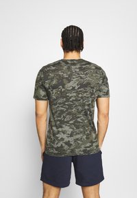 Zelené maskáčové tričko vyrobené z měkké látky, s kulatým výstřihem a krátkými rukávy, s texturovaným vzorem po celém povrchu.