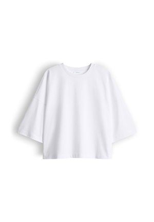 T-shirt bianca oversize a maniche corte con scollo rotondo, spalle scese e vestibilità ampia, distesa su uno sfondo bianco.