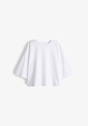 T-shirt bianca oversize a maniche corte con scollo rotondo, spalle scese e vestibilità ampia, distesa su uno sfondo bianco.