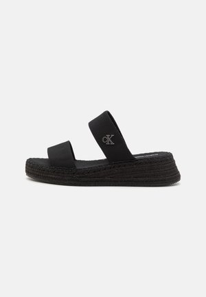 Mustat espadrillet sandaalit, joissa on kaksinkertaiset kangashihnat, punottu juutti-pohja ja hienovarainen logo-yksityiskohta yhdellä hihnalla. Tasainen kumipohja.