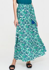 Spódnica maxi z niebiesko-zielonym wzorem tropikalnych liści, o warstwowym kroju i teksturowanej tkaninie. Zawiera dekoracyjną niebieską frędzelkę w talii.