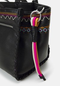 Černá kožená taška s barevným vyšívaným lemem a stříbrným kroužkem, který drží růžové, bílé a žluté šňůrky svázané černou kůží.