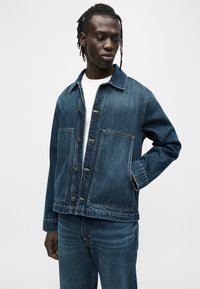 Τζιν μπουφάν σε σκούρο μπλε με κουμπιά και δύο μπροστινές τσέπες. Διαθέτει κλασικό γιακά και ίσια γραμμή.