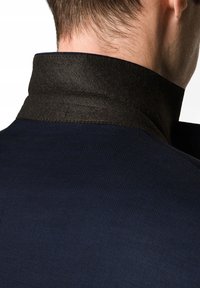 Granatowa kurtka z kontrastującym ciemnym filcowym kołnierzem, teksturowanym materiałem i zbliżeniowym ujęciem szwów na kołnierzu.