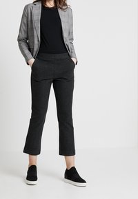 Blazer a quadri grigi con un design aderente, abbinato a pantaloni tapered grigio scuro e sneakers nere slip-on. Tessuto morbido in tutta la sua lunghezza.