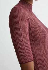 Särmikkäästä ja istuvasta topista syvän viininpunaisena, jossa on lyhyet hihat. Valmistettu kiiltävästä, teksturoidusta kankaasta, jossa korkea pyöreä kaulus.