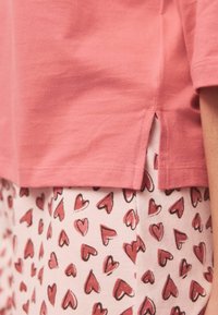 Bomuldspyjamasæt med en lyserød kortærmet top med sideslidser, kombineret med hvide bukser med mønster af røde hjerter.
