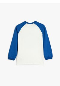 Valkoinen paita sinisillä raglan-hihoilla; pitkät hihat, pyöreä kaula-aukko ja pehmeä textura; ei näkyviä grafiikoita tai kuvioita.