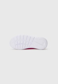 Semelle en caoutchouc texturé blanc avec motif en grille et logo Nike sur la semelle rose, contre un fond clair uni.