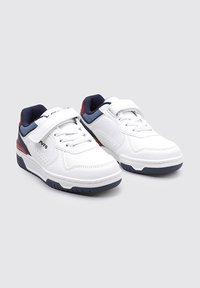 Zapatillas deportivas blancas con parte superior sintética suave, acentos en azul marino, correa de velcro y suela de goma texturizada. Presentan un costado perforado para mayor transpirabilidad.