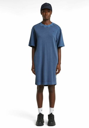 Denim dress in dark blue, short sleeves, crew neck, and relaxed fit. Worn with a matching cap and black sneakers. White socks visible.