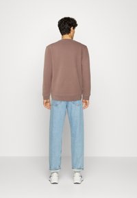 Sudadera marrón de manga larga, cuello redondo y puños de canalé, combinada con unos vaqueros holgados de color azul claro. Modelo de espaldas, de pie sobre un fondo blanco.