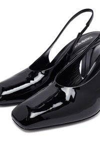 Zapatos de tacón de charol negro con punta cuadrada y tacones de bloque, mostrando una superficie brillante y lisa y correas traseras abiertas.