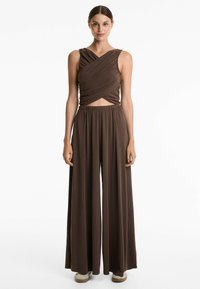 Salopette marron avec un haut sans manches croisé à l'avant et un pantalon large à taille élastique, fabriquée en tissu doux et drapé.