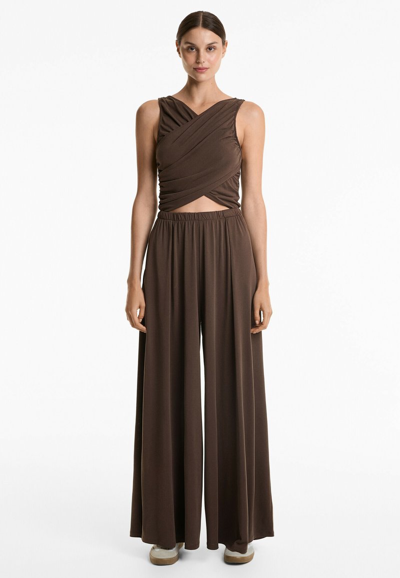 Salopette marron avec un haut sans manches croisé à l'avant et un pantalon large à taille élastique, fabriquée en tissu doux et drapé.