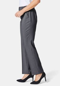 Graue maßgeschneiderte Hose mit entspannter Passform, Seitentaschen und elastischem Bund, kombiniert mit schwarzen spitzen Absatzschuhen.