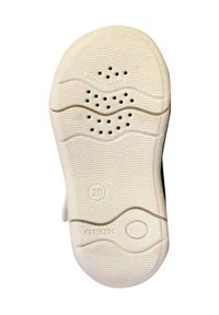 Suela de zapato blanca con patrones de olas texturizados, agujeros de ventilación y un logotipo circular. Talla 20 indicada cerca del talón.