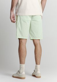 Lichtgroene shorts met een relaxte pasvorm, gemaakt van een gladde stof. In combinatie met witte sneakers en crèmekleurige sokken.