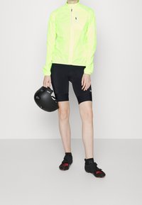 Veste réfléchissante jaune vif, shorts de cyclisme noirs et casque noir. Chaussures avec des accents rouges. Conception axée sur la performance avec une coupe ajustée.