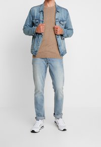Jeansjacke, beigefarbener Pullover, hellblaue Jeans und weiße Sneakers mit schwarzen Akzenten. Einfaches, lässiges Layering mit klassischen Materialien.