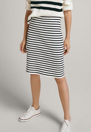 Femme portant une jupe rayée horizontale noire et blanche, des baskets blanches et un pull crème avec des rayures noires.